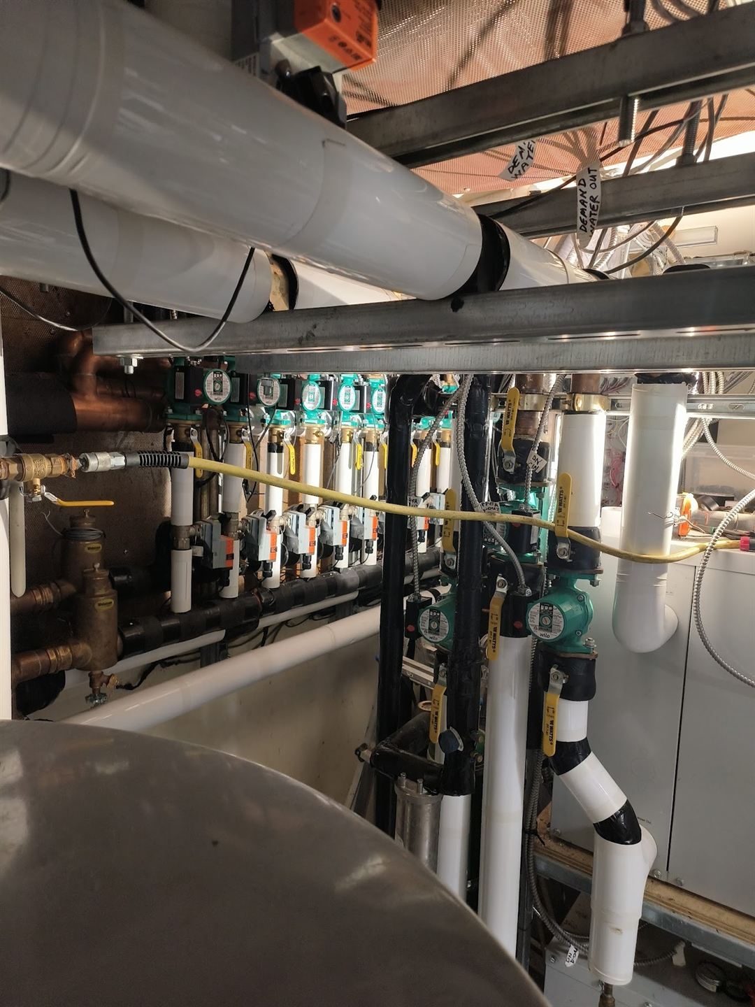 A ceiling-mounted mechanical manifold: insulated mains, isolation valves, green-topped balancing valves and branch takeoffs running along a concrete ceiling.