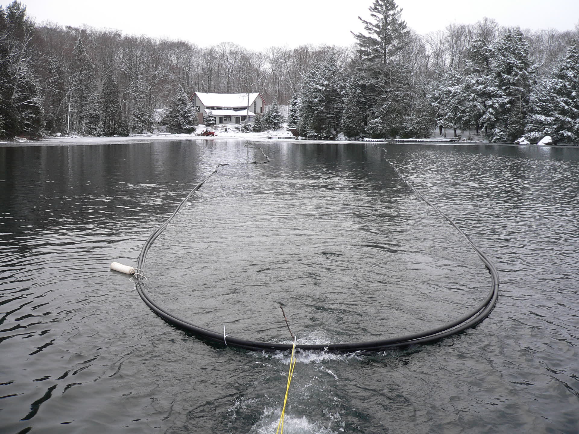 A geothermal lake loop being towed into position on a lake in winter, before it is sunk