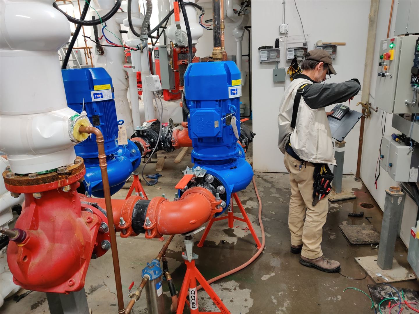 Blue vertical loop circulators and red suction diffusers piped into a central plant, with a technician working at a control panel behind them.