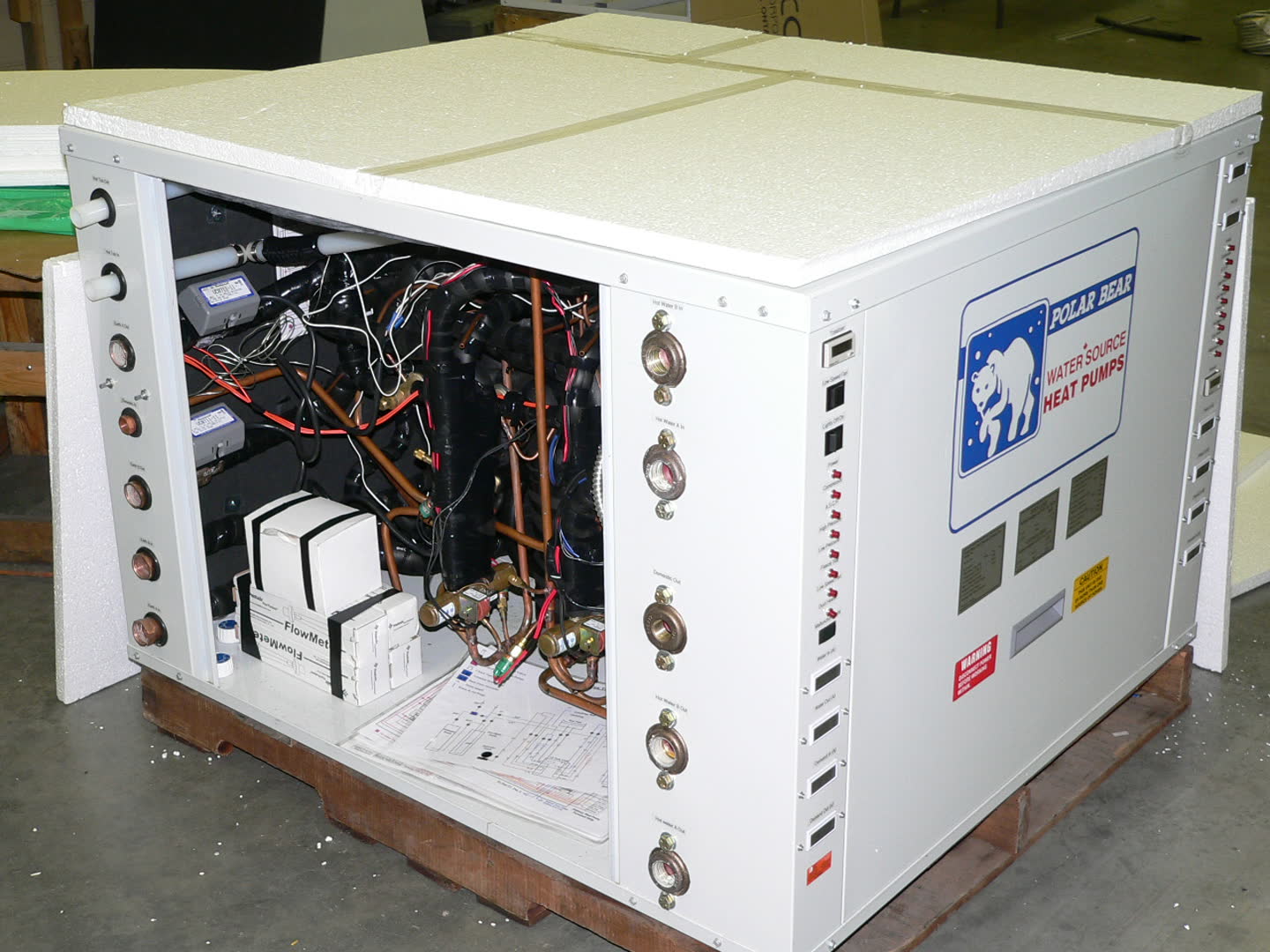 Polar Bear cabinet open on the shop floor, compressors, copper, flow-meter cartons and a wiring diagram on the pallet.